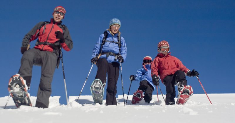 A family of four enjoys a snowshoeing excursion on a bright, sunny day.
