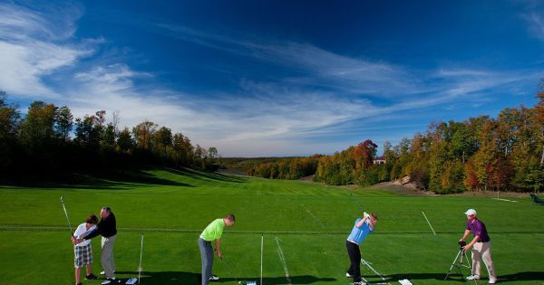 Two PGA Professional Instructors work with three golfers at the Treetops Resort driving range.