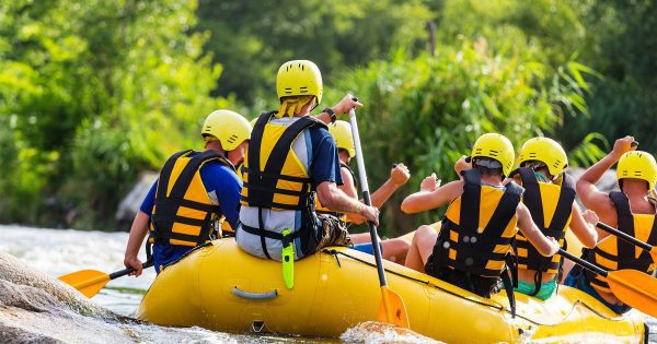 A group of people in full safety gear participate in a rafting excursion on a river.