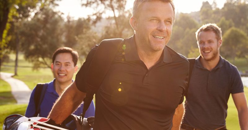 Three smiling men on a golf course on a sunny day