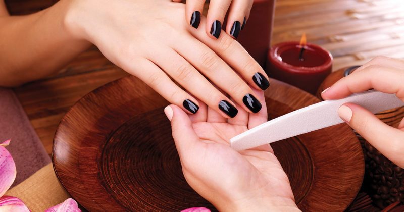 Woman's hands with dark nail polish receiving manicure