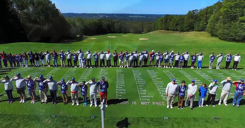 large group of golfers standing in formation around large names of fallen soldiers