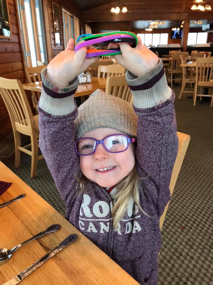 Smiling young girl wearing glasses, a wool hat and purple sweatshirt holding bracelets