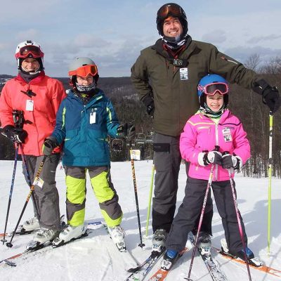 Family of 4 on skis at the top of a ski hill