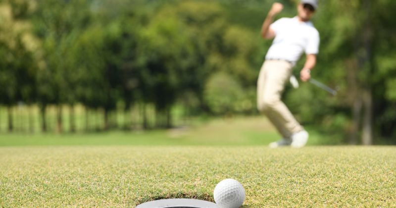 Golf ball rests next to hole as man in background reacts