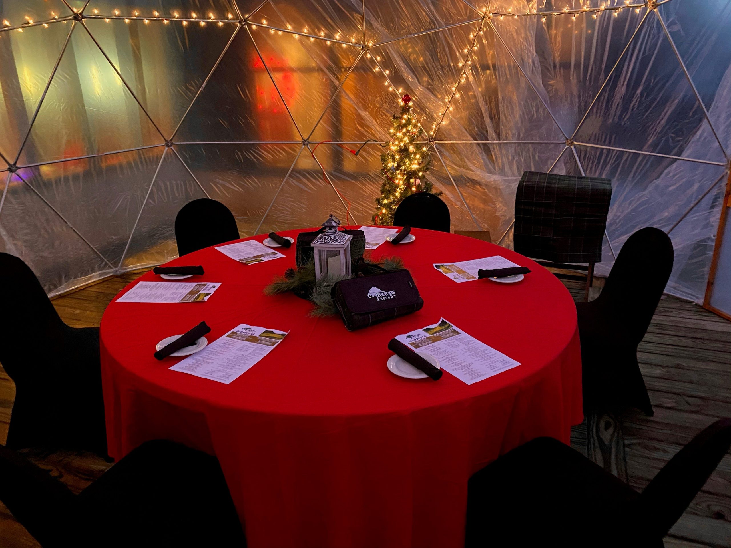 A dining igloo at Treetops Resort with red tablecloth, string lights, and space for six family members to enjoy a delicious meal.