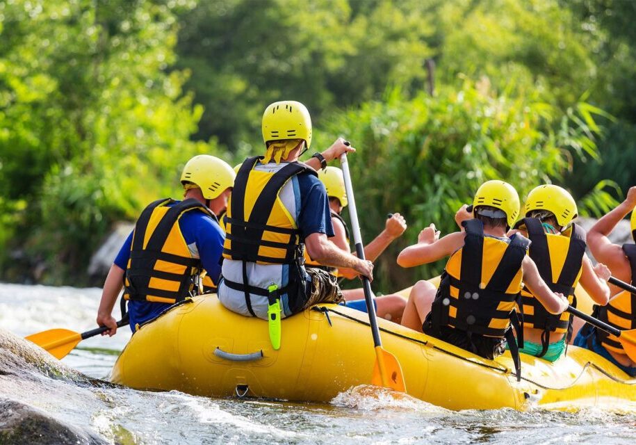 A group of people in full safety gear participate in a rafting excursion on a river.